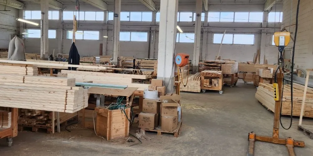 The production hall: stacked boards, timber on wheeled trolleys, boxes on a pallet and a hoist