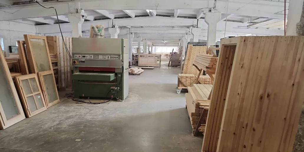 A sanding machine in a long workshop, with glazed timber window frames on the left and timber door leaves on the right