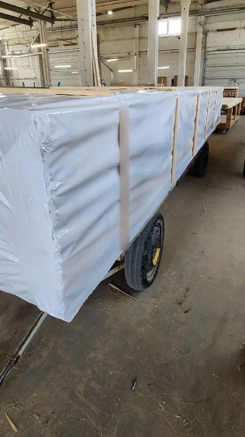 A kit packed in white film, with timber battens along its side, on a wheeled workshop trolley