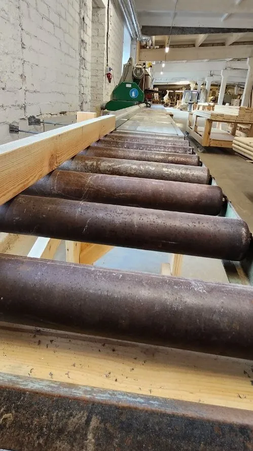 A timber beam on a roller table leading towards a machine in a long workshop