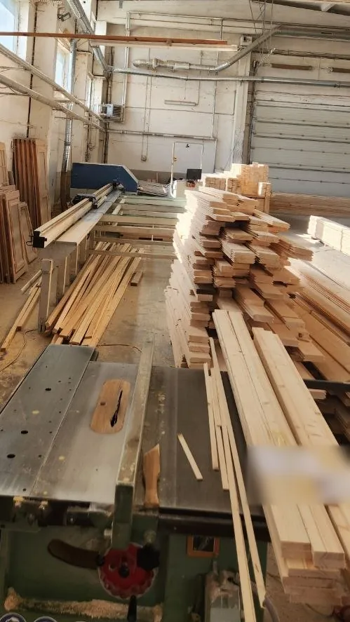 A table saw in front of stacked boards and battens, with timber frames against the wall behind