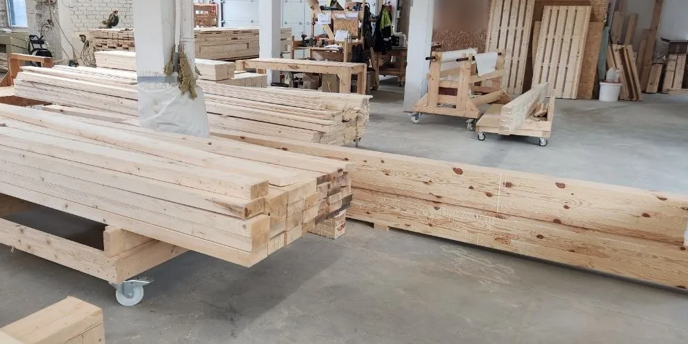 Stacks of sawn beams on wheeled trolleys, and a long run of beams on the floor with pencil marks on them